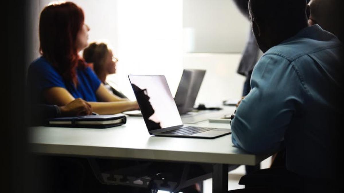 Students sitting at a desk, looking up at the instructor.