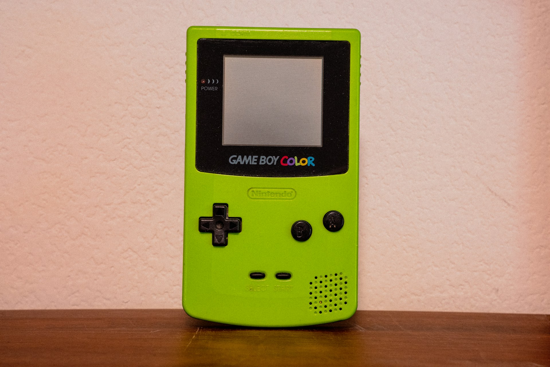 A green gameboy color rests against a wall.